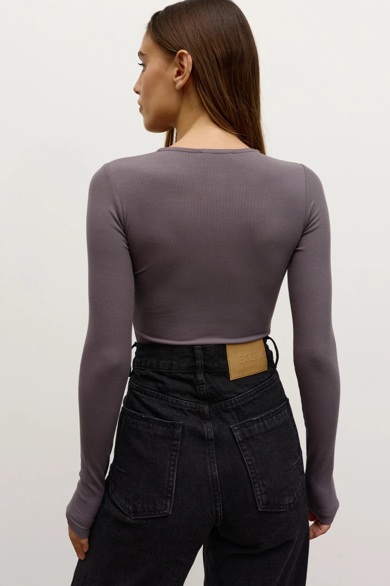 Woman wearing a long-sleeve purple top and black pants on a plain background