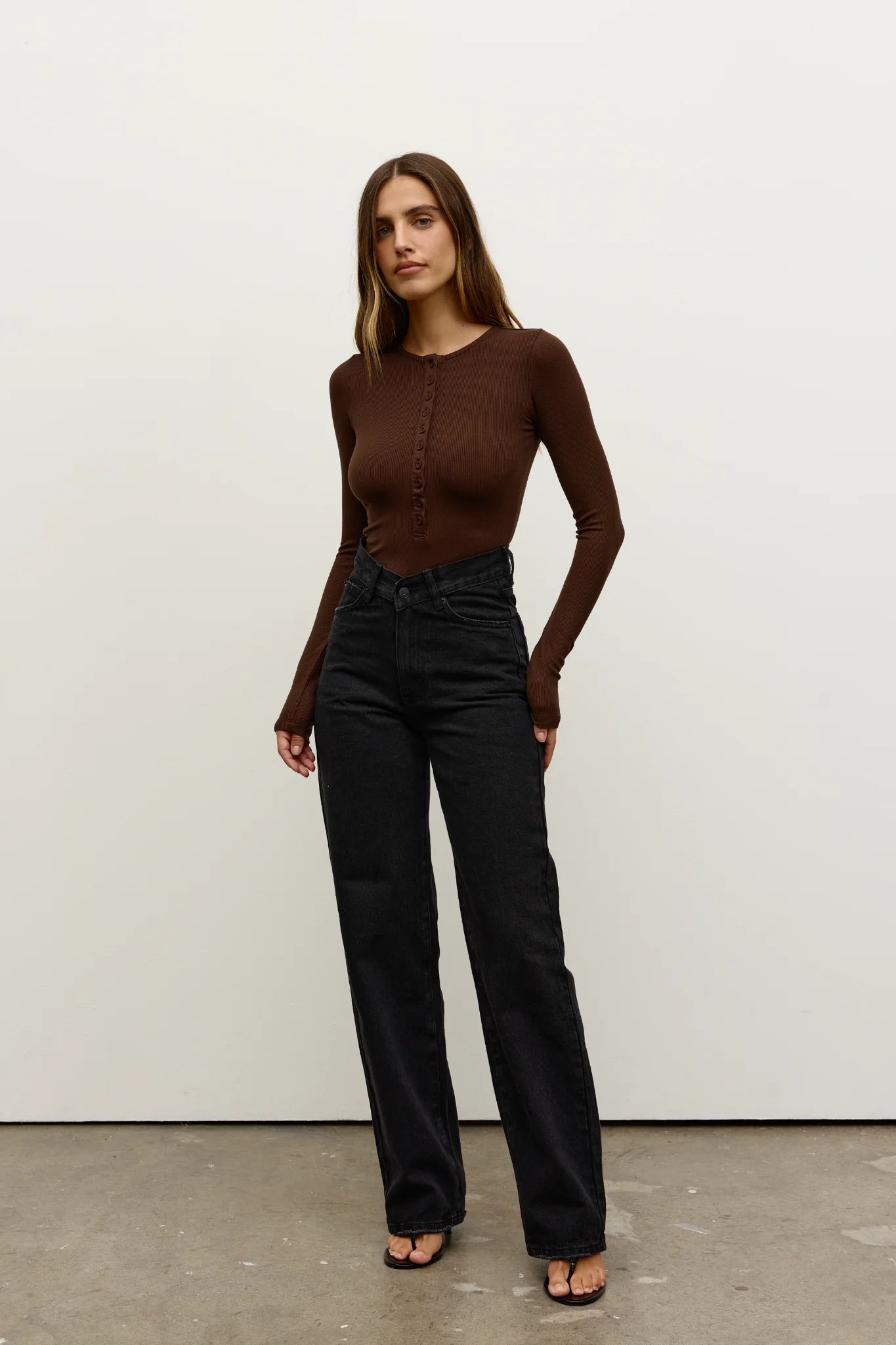 Woman wearing a brown top and black pants against a white background