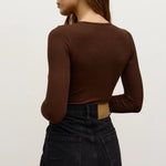 Person wearing a brown long-sleeve top and black pants on a light background