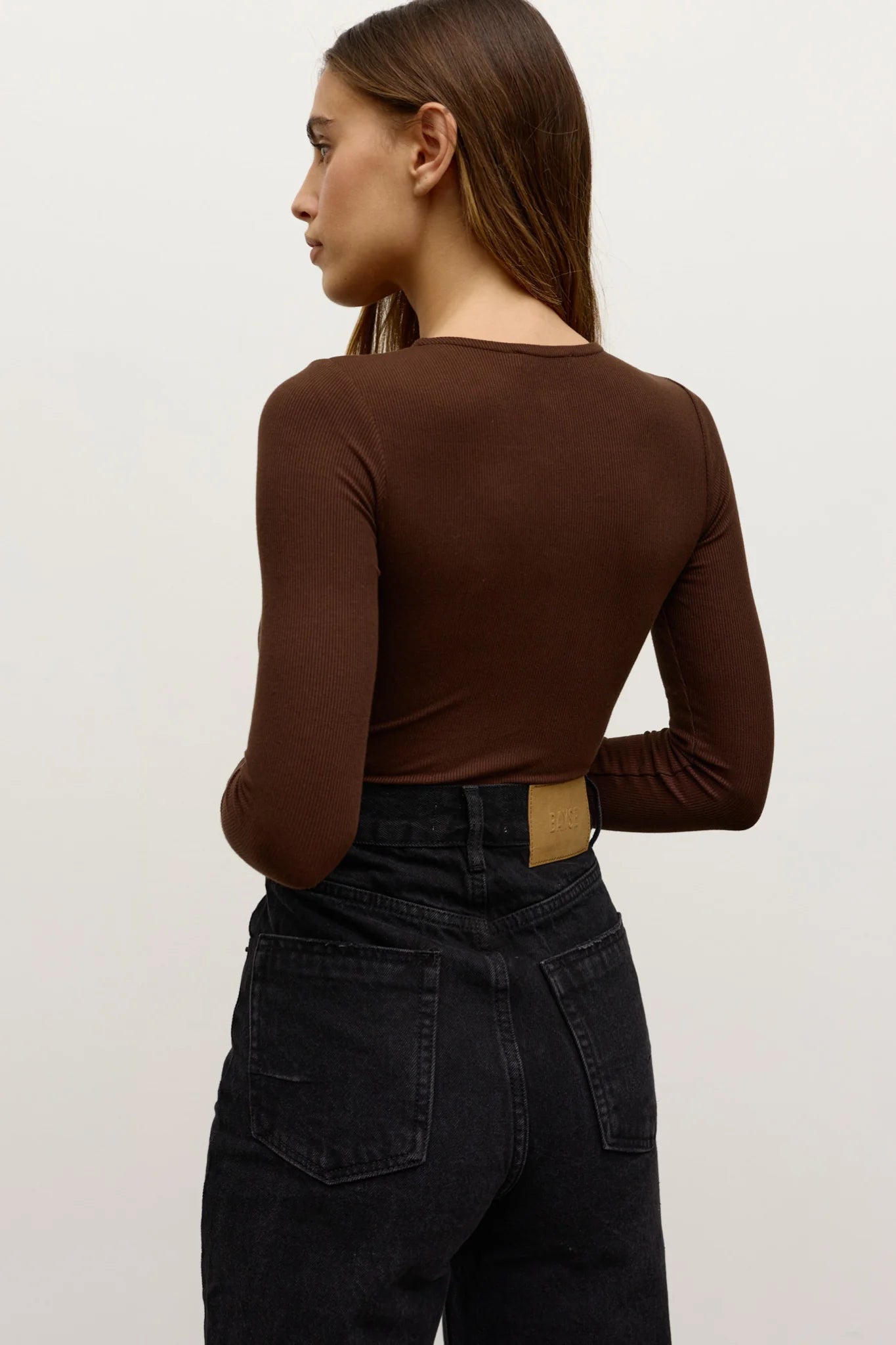 Person wearing a brown long-sleeve top and black pants on a light background