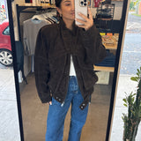 Person taking a mirror selfie wearing a brown jacket and blue jeans in an indoor setting.
