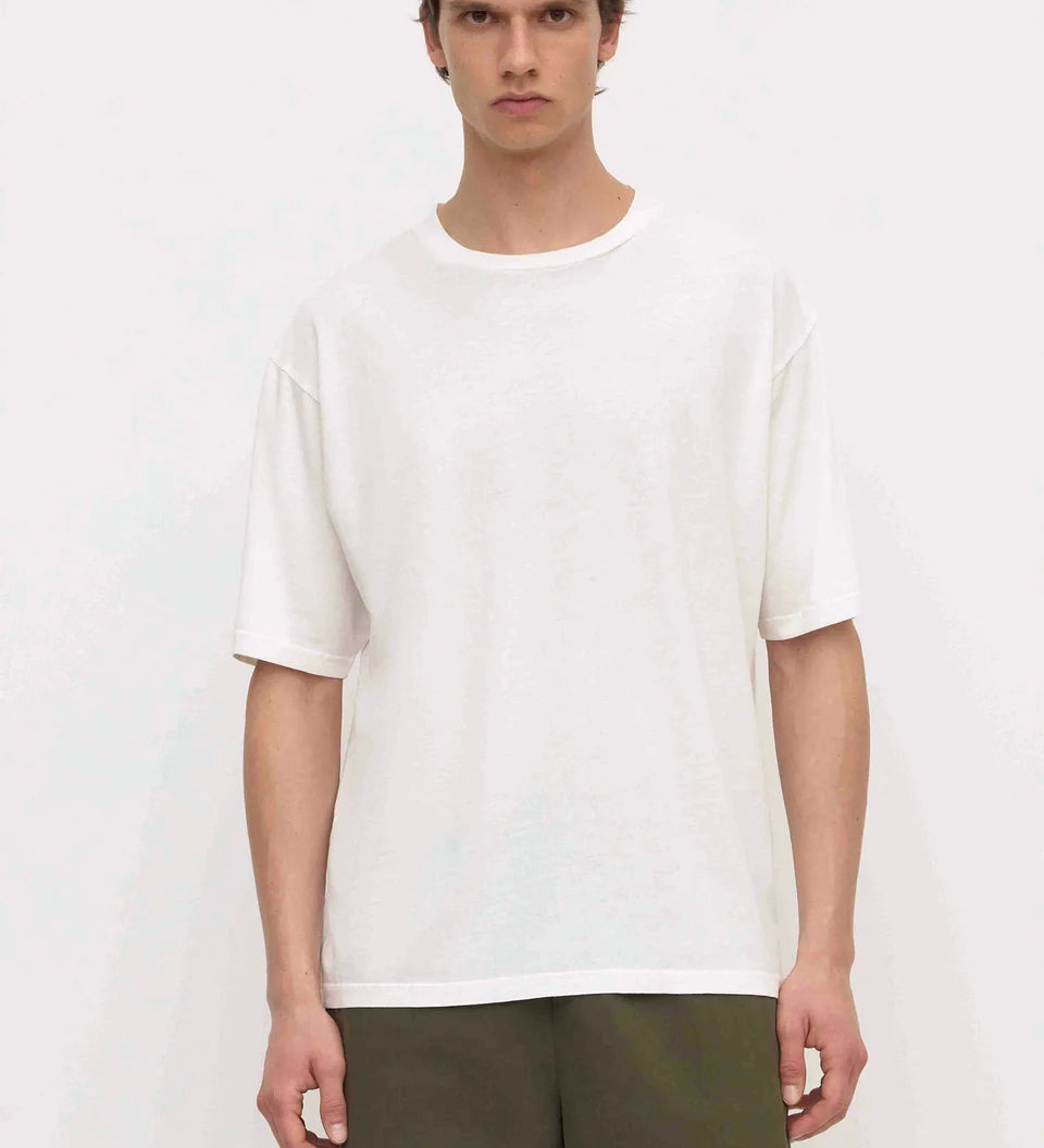 A man wearing a plain white short-sleeve crewneck t-shirt and olive green pants, standing against a light off-white background.