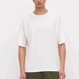 A man wearing a plain white short-sleeve crewneck t-shirt and olive green pants, standing against a light off-white background.