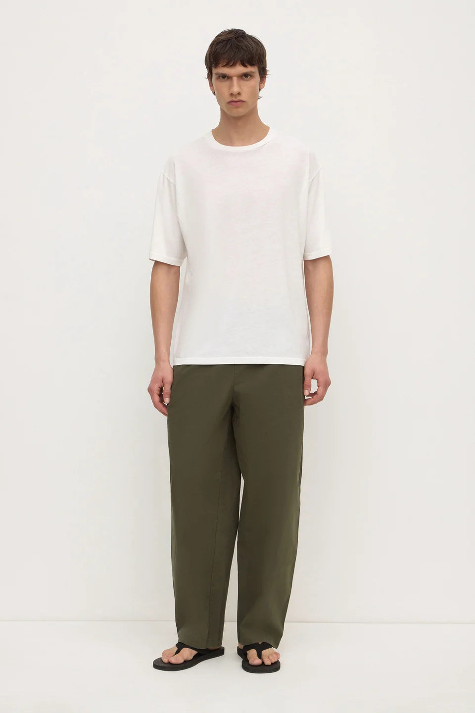 A man modeling a white short-sleeve crewneck t-shirt and olive green wide-leg trousers, standing against a plain white studio background.