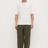 A man modeling a white short-sleeve crewneck t-shirt and olive green wide-leg trousers, standing against a plain white studio background.