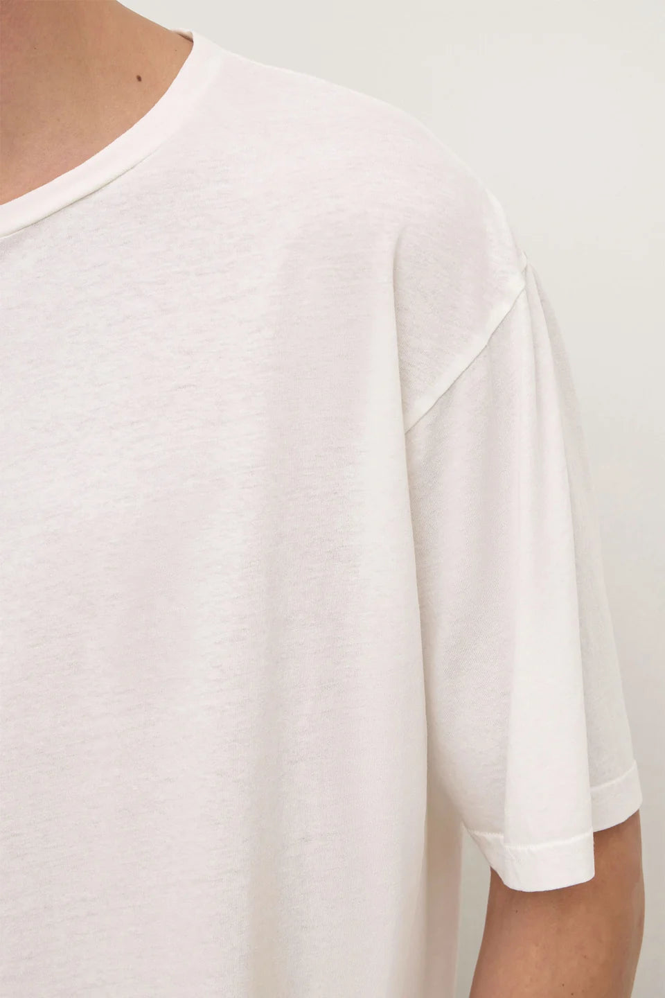 Close-up of a person wearing an oversized white short-sleeve crewneck t-shirt against a plain light background.