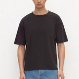A man wearing a dark charcoal gray crewneck t-shirt and light blue jeans, standing against a plain white studio background.