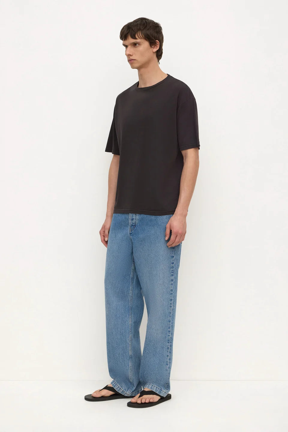A man modeling a black short-sleeve crewneck t-shirt and wide-leg light blue jeans, standing against a plain white studio background.