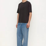 A man modeling a black short-sleeve crewneck t-shirt and wide-leg light blue jeans, standing against a plain white studio background.