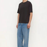 A man modeling a black short-sleeve crewneck t-shirt and wide-leg light blue jeans, standing against a plain white studio background.