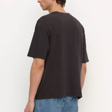 A man wearing a dark charcoal gray oversized t-shirt and blue jeans, shown from a side-back angle against a plain white studio background.