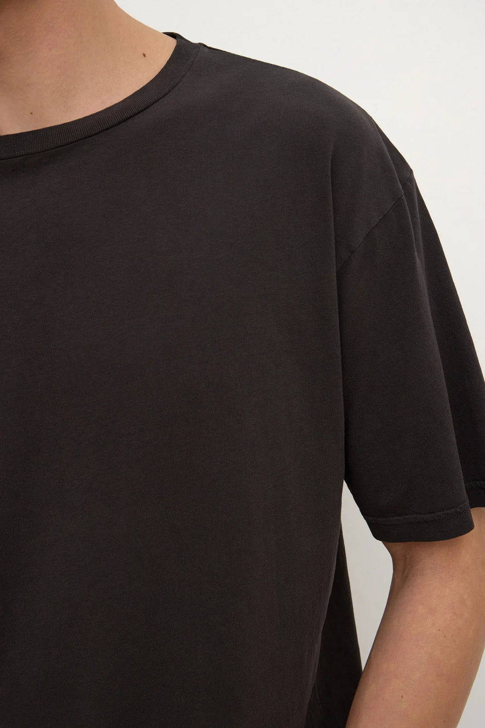 Close-up of a person wearing a plain black short-sleeve crew-neck T-shirt against a light neutral background.