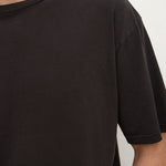 Close-up of a person wearing a plain black short-sleeve crew-neck T-shirt against a light neutral background.