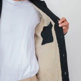 Person holding a black coat with beige interior against a white background