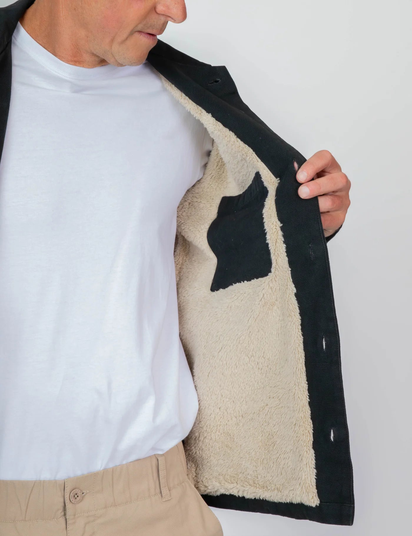Person holding a black coat with beige interior against a white background
