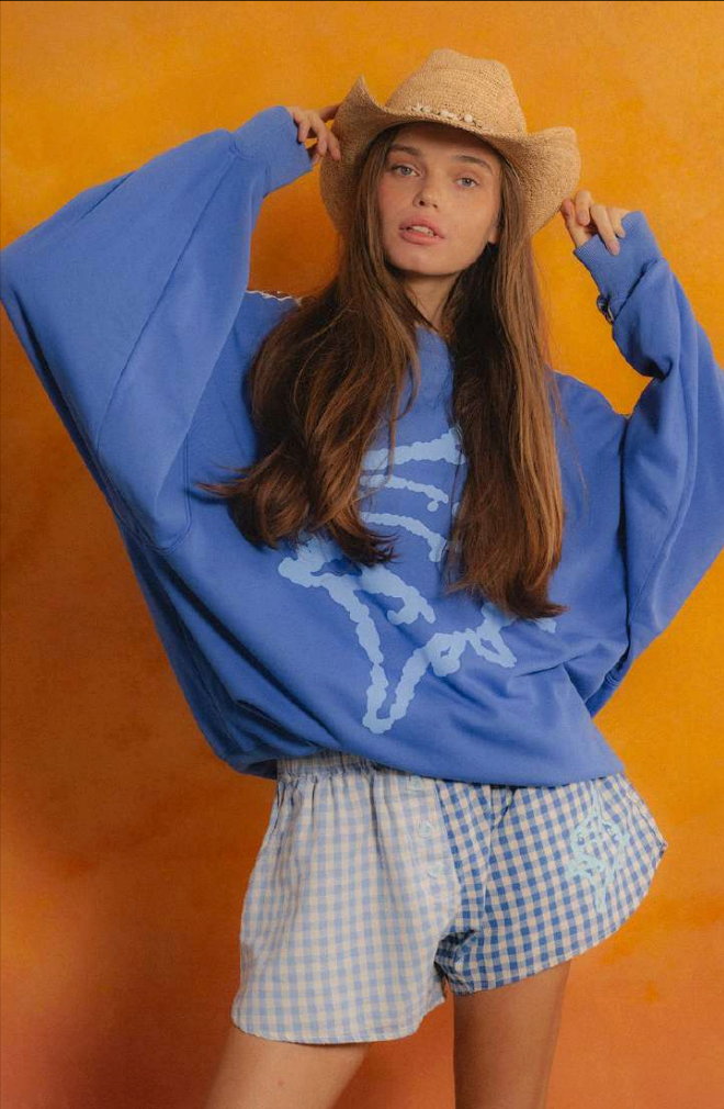 Person wearing a blue sweatshirt with a graphic design and checkered shorts against an orange background