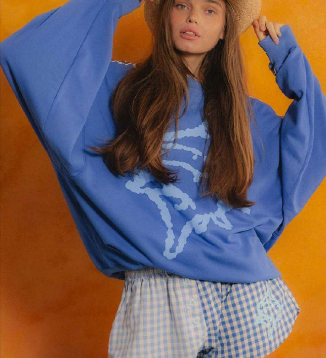 Person wearing a blue sweatshirt with a graphic design and checkered shorts against an orange background