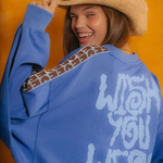 Person wearing a blue sweatshirt with text and patterns, smiling against an orange background