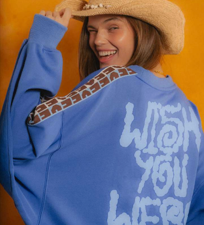 Person wearing a blue sweatshirt with text and patterns, smiling against an orange background