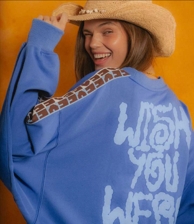 Person wearing a blue sweatshirt with text and patterns, smiling against an orange background