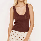 A blonde model wearing a brown ribbed knit scoop-neck tank top with scalloped edges and a cream mini skirt with brown polka dots, set against a plain white studio background.