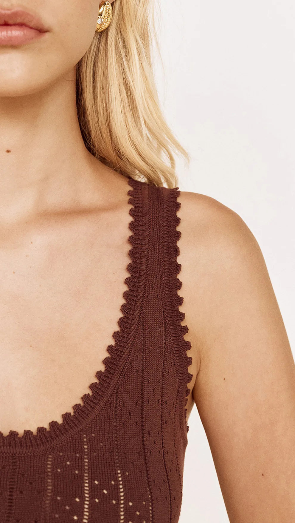 Close-up of a model wearing a dark brown knit top with a distinctive scalloped scoop neckline and textured eyelet pattern.