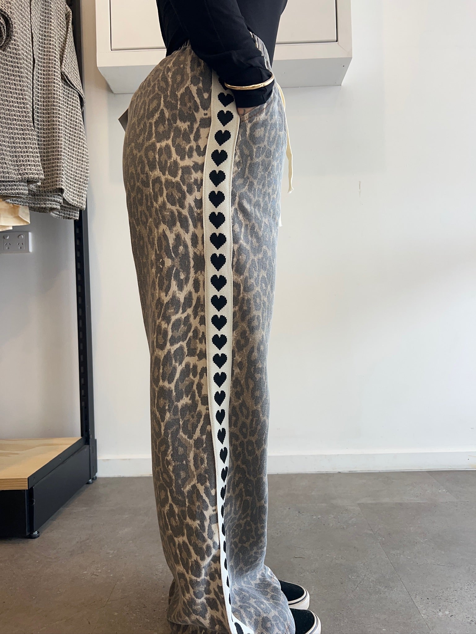 Person wearing leopard print pants with heart pattern on a plain background
