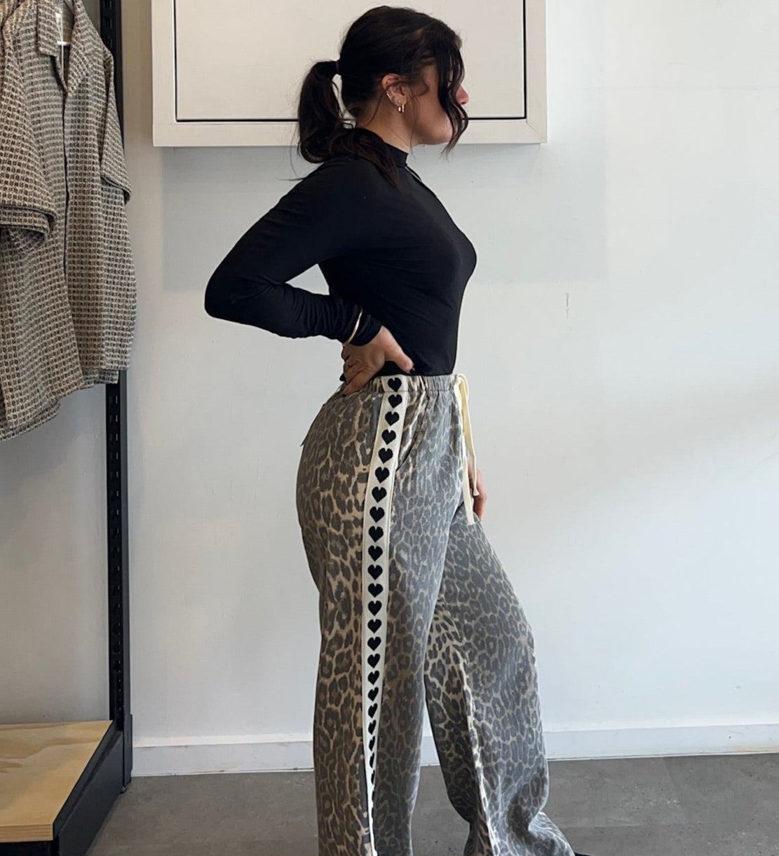 Person wearing a black top and patterned pants standing in a room with a rack of clothes and a whiteboard on the wall.
