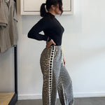 Person wearing a black top and patterned pants standing in a room with a rack of clothes and a whiteboard on the wall.