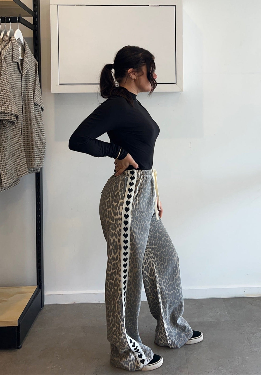 Person wearing a black top and patterned pants standing in a room with a rack of clothes and a whiteboard on the wall.