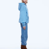 A model is shown from the back wearing a light blue oversized hoodie, blue jeans, and brown heeled ankle boots against a plain white studio background.