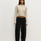 Woman wearing a beige sweater and black pants against a white background