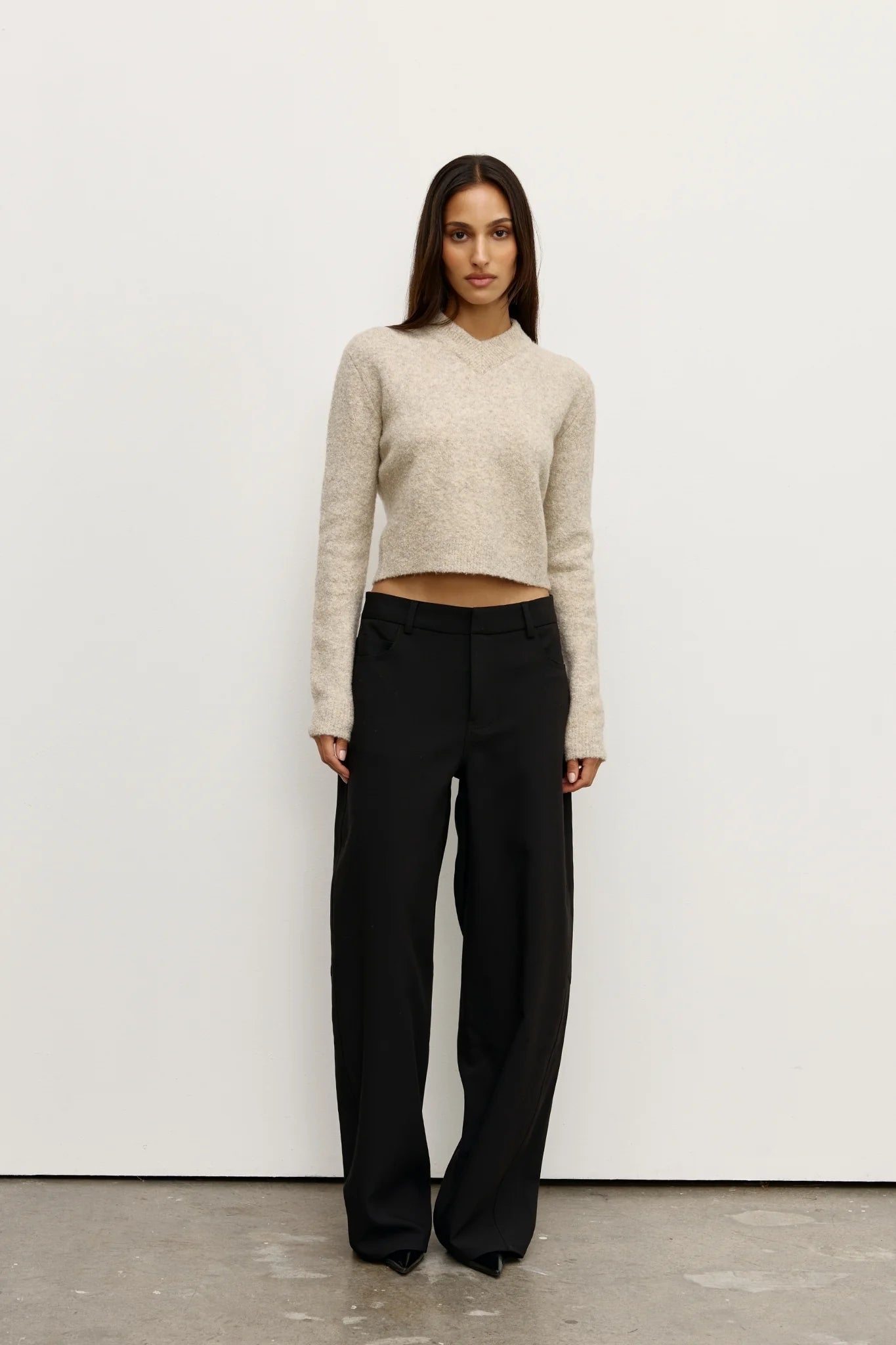Woman wearing a beige sweater and black pants against a white background