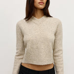 Woman wearing a beige sweater and black pants against a white background