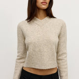 Woman wearing a beige sweater and black pants against a white background