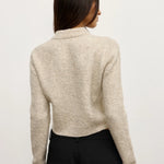 Person wearing a beige sweater and black pants on a plain background