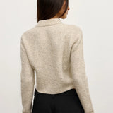 Person wearing a beige sweater and black pants on a plain background