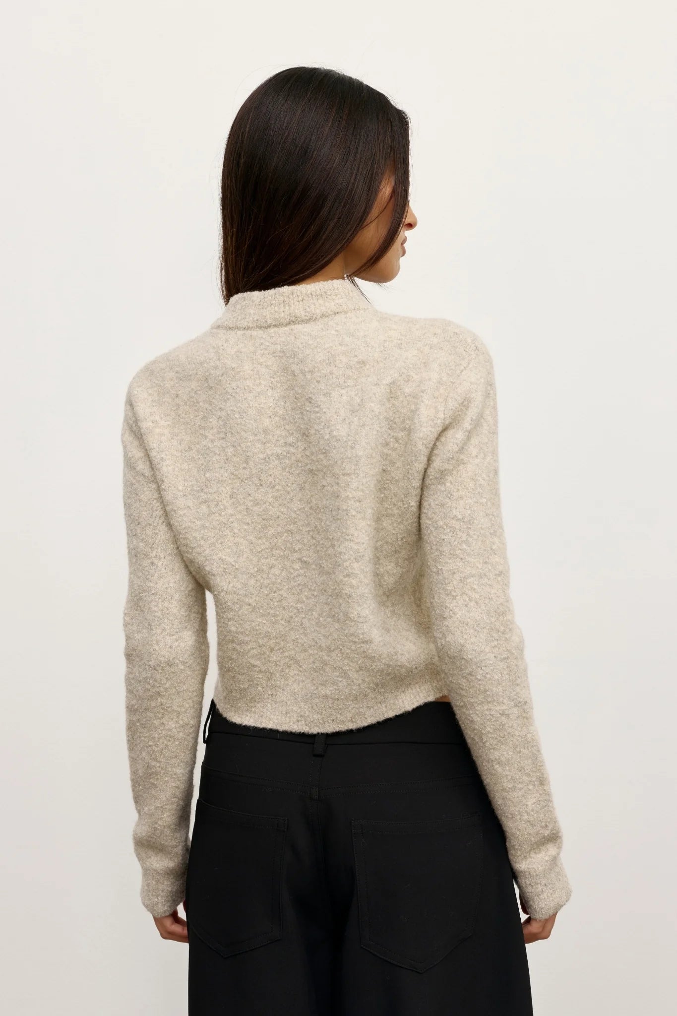 Person wearing a beige sweater and black pants on a plain background