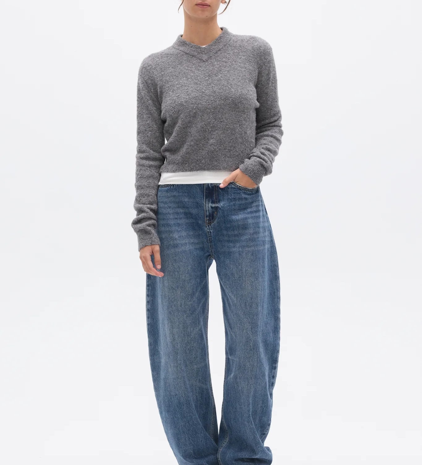 Person wearing a gray sweater and blue jeans on a white background