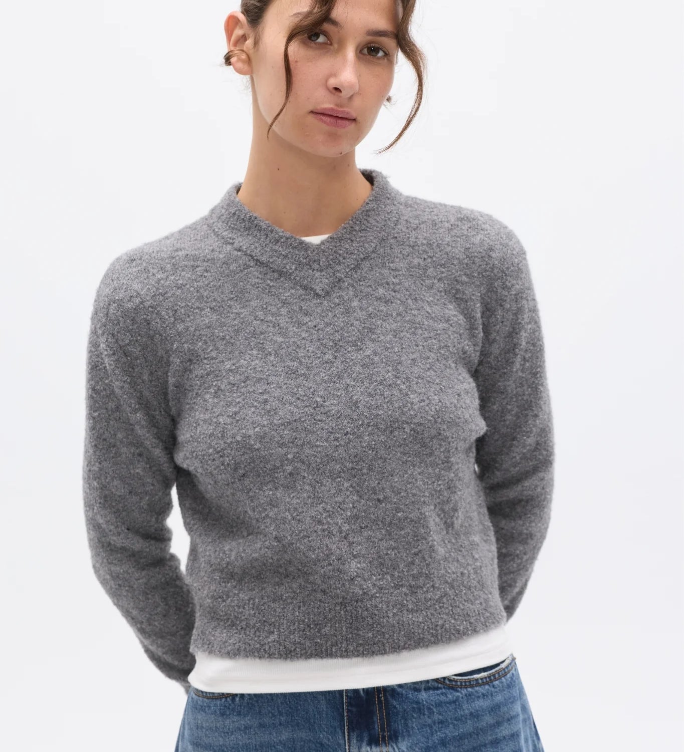 Woman wearing a gray sweater and blue jeans on a white background