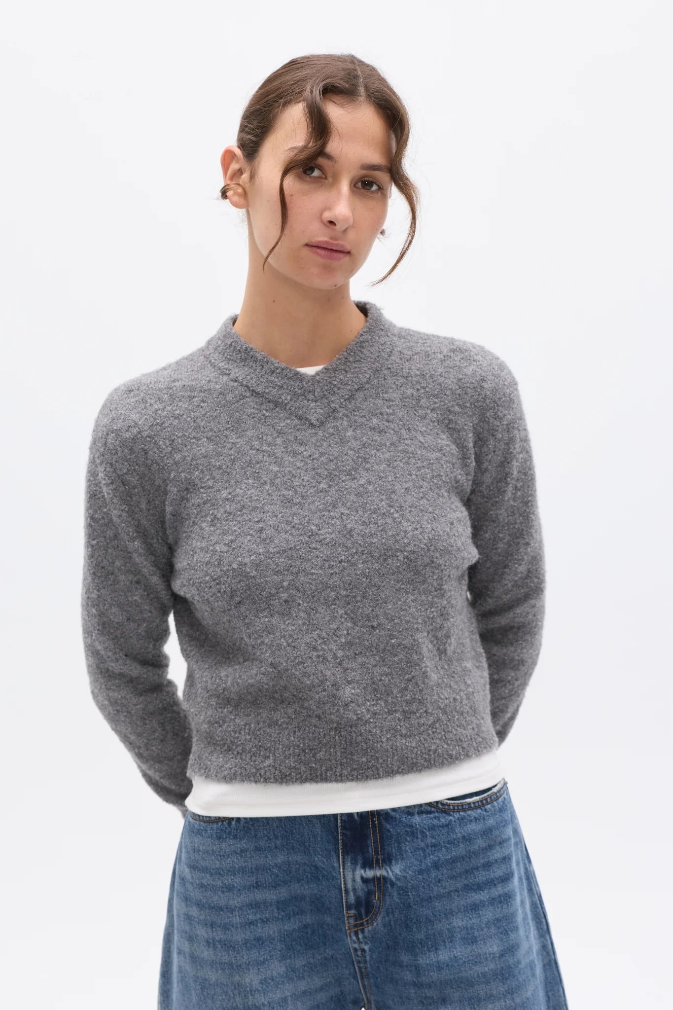 Woman wearing a gray sweater and blue jeans on a white background