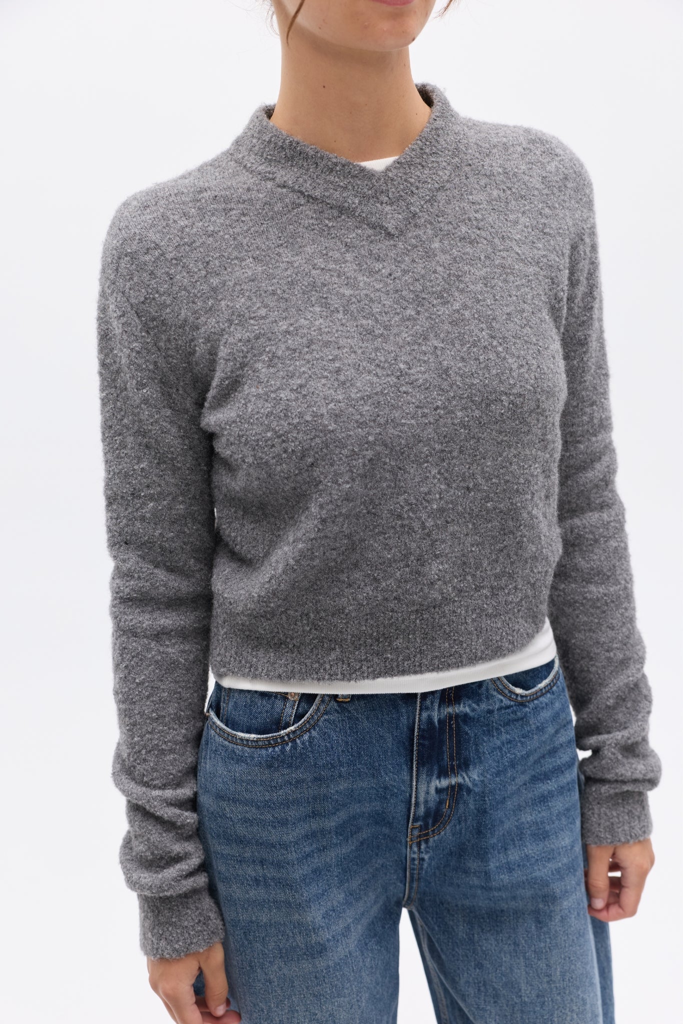 Person wearing a gray sweater and blue jeans on a white background