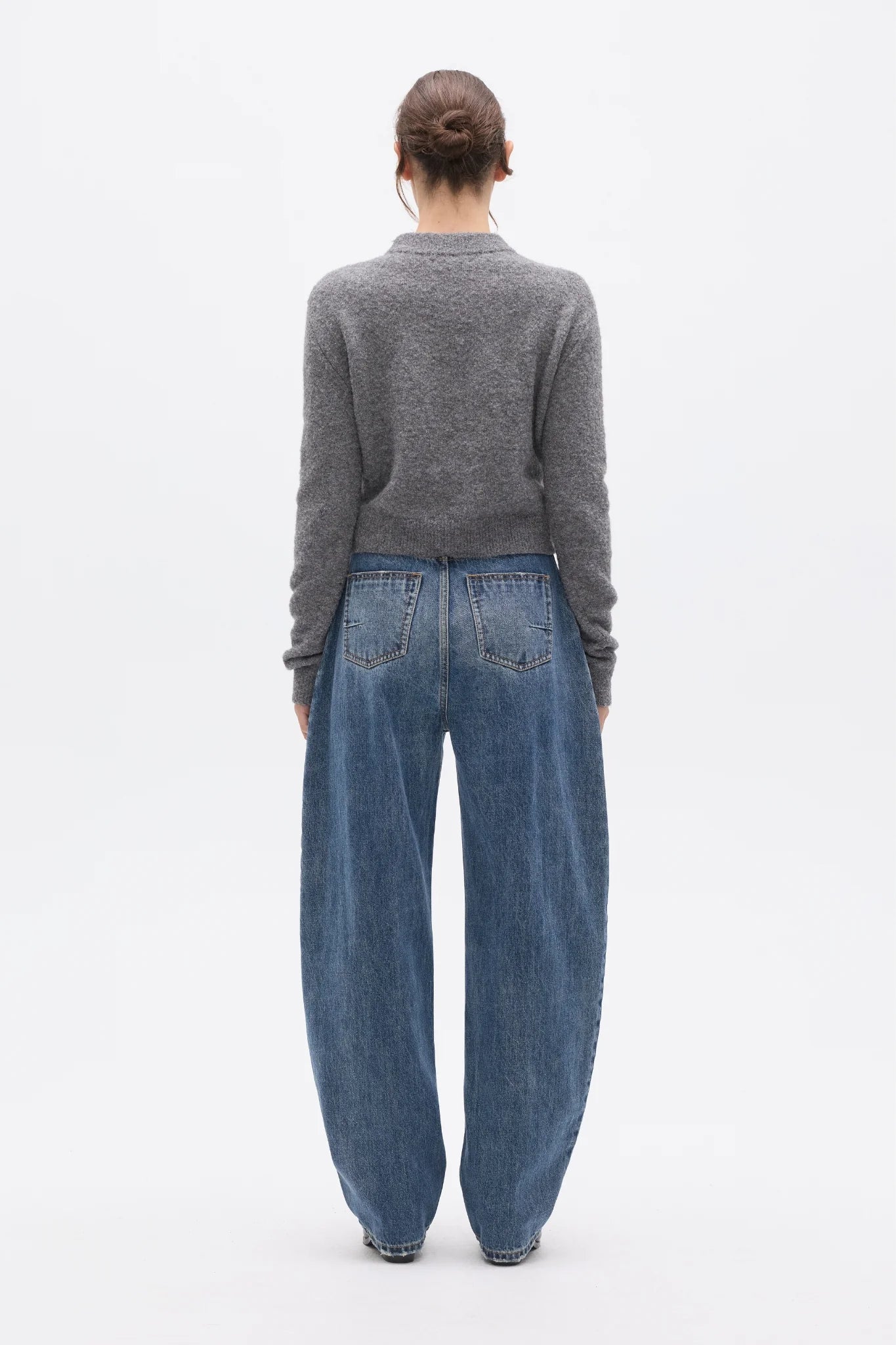 Person wearing a gray sweater and blue jeans on a white background