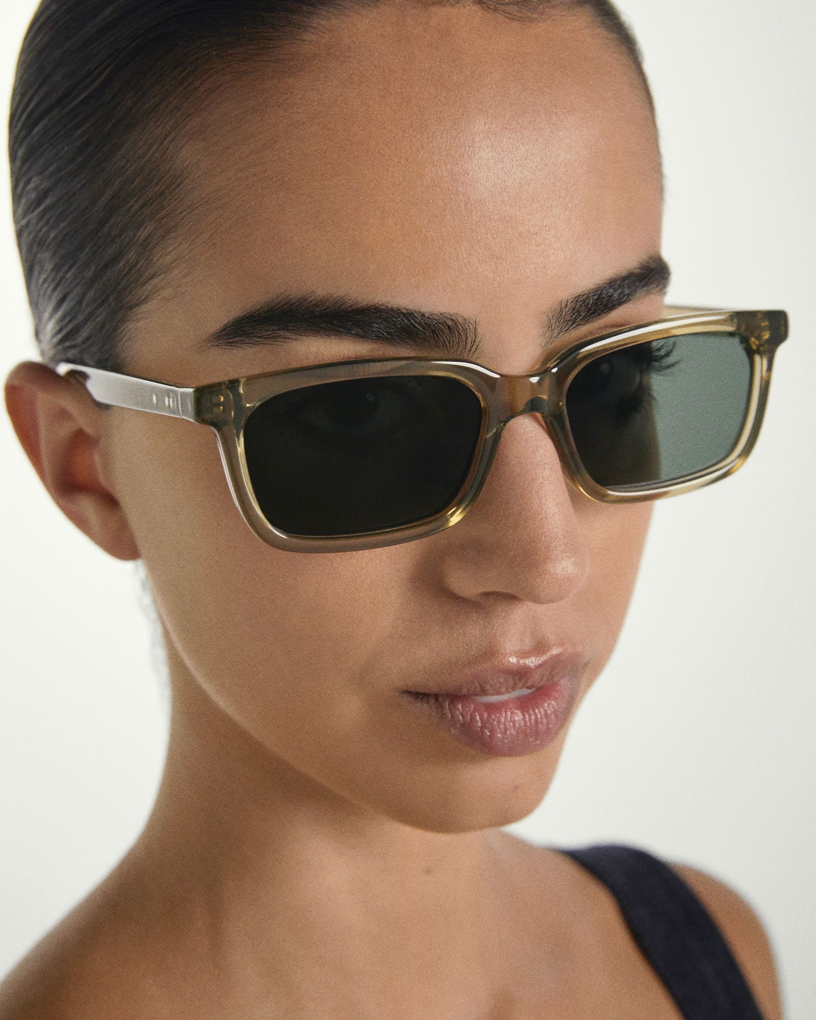 Close-up of a person wearing Sage framed sunglasses with a neutral background
