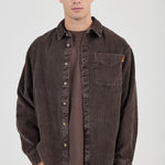Man wearing a brown corduroy shirt over a brown t-shirt on a white background