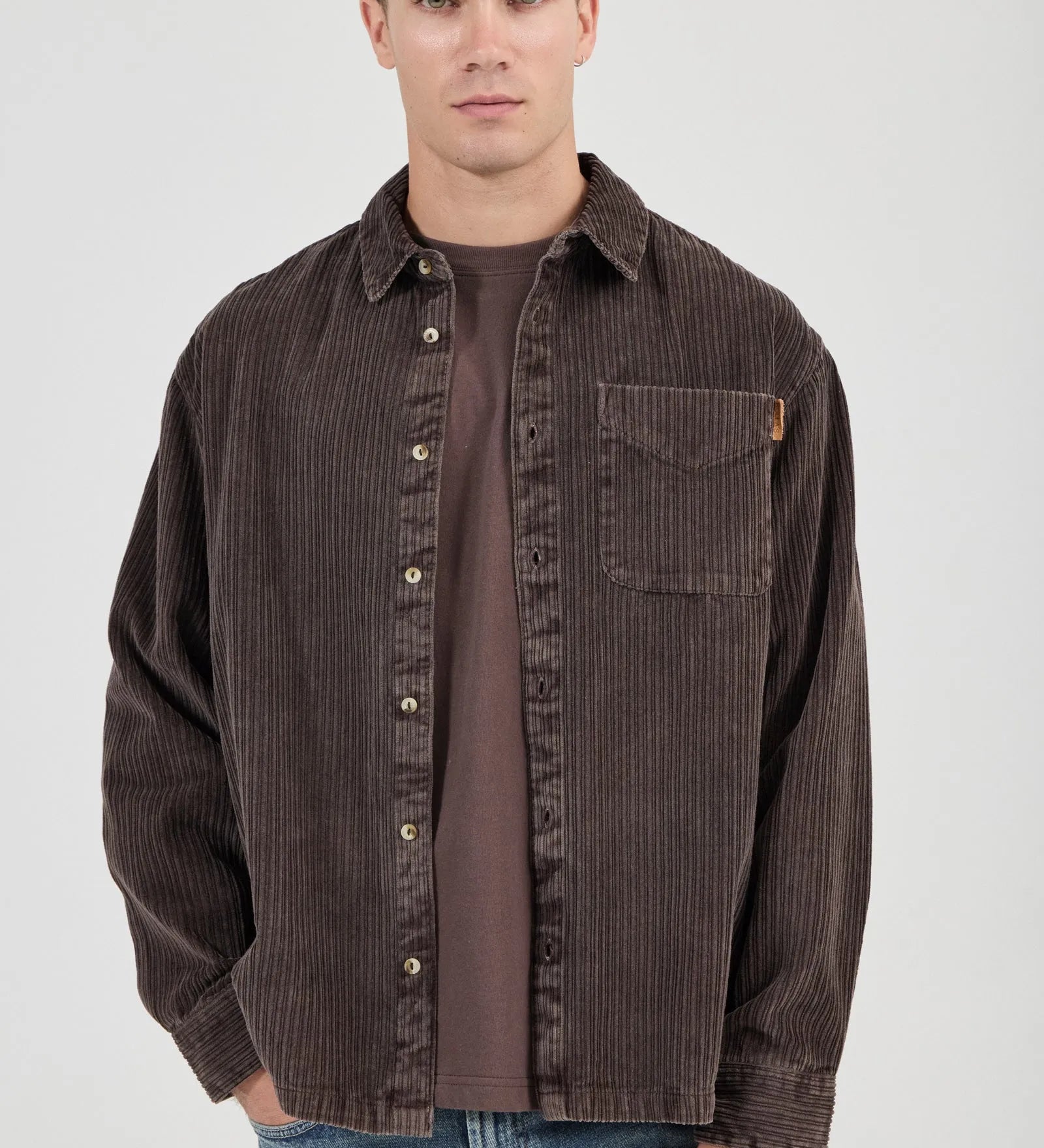 Man wearing a brown corduroy shirt over a brown t-shirt on a white background