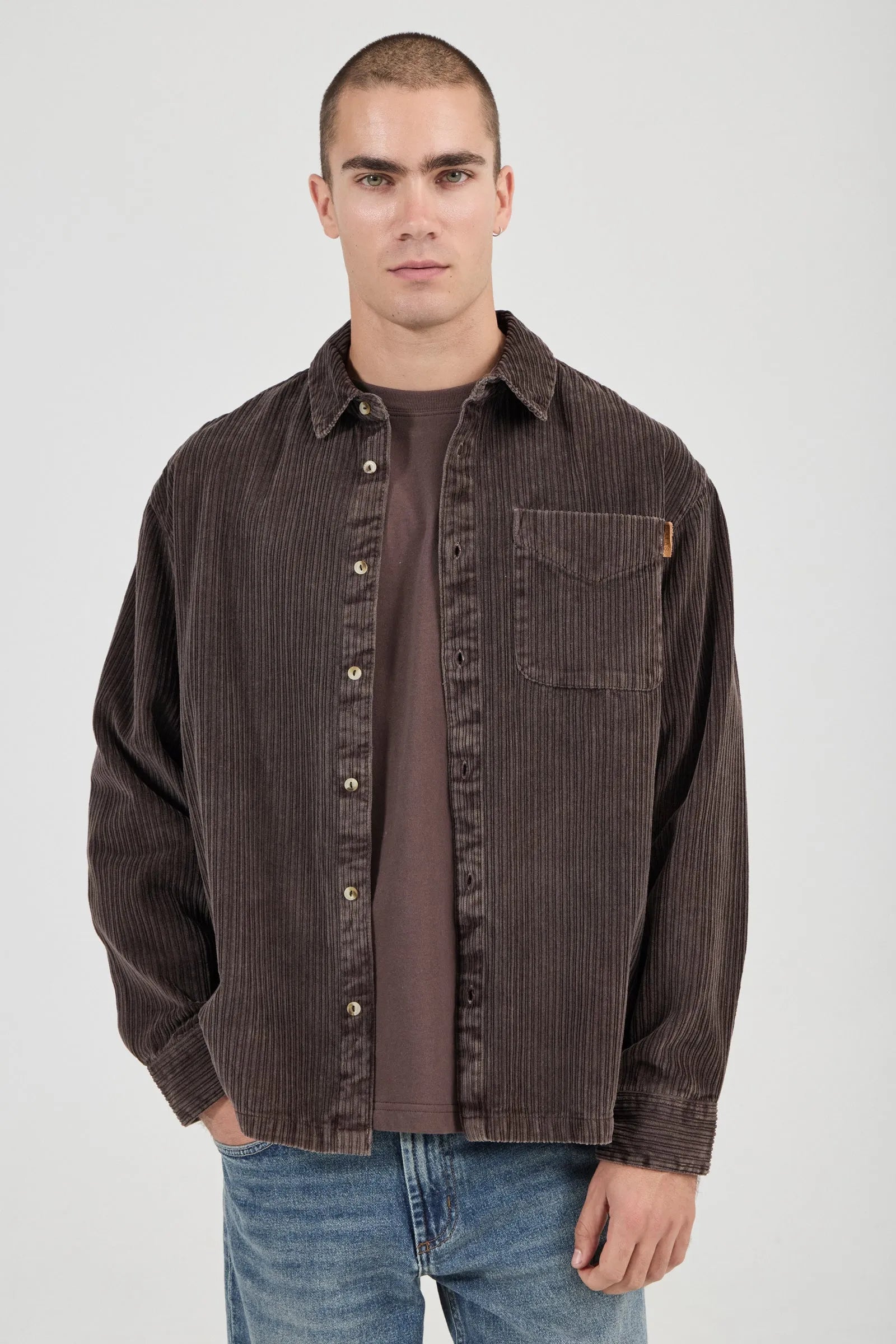 Man wearing a brown corduroy shirt over a brown t-shirt on a white background