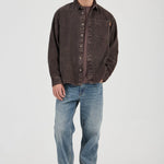 Man wearing a brown button-up shirt and blue jeans on a white background