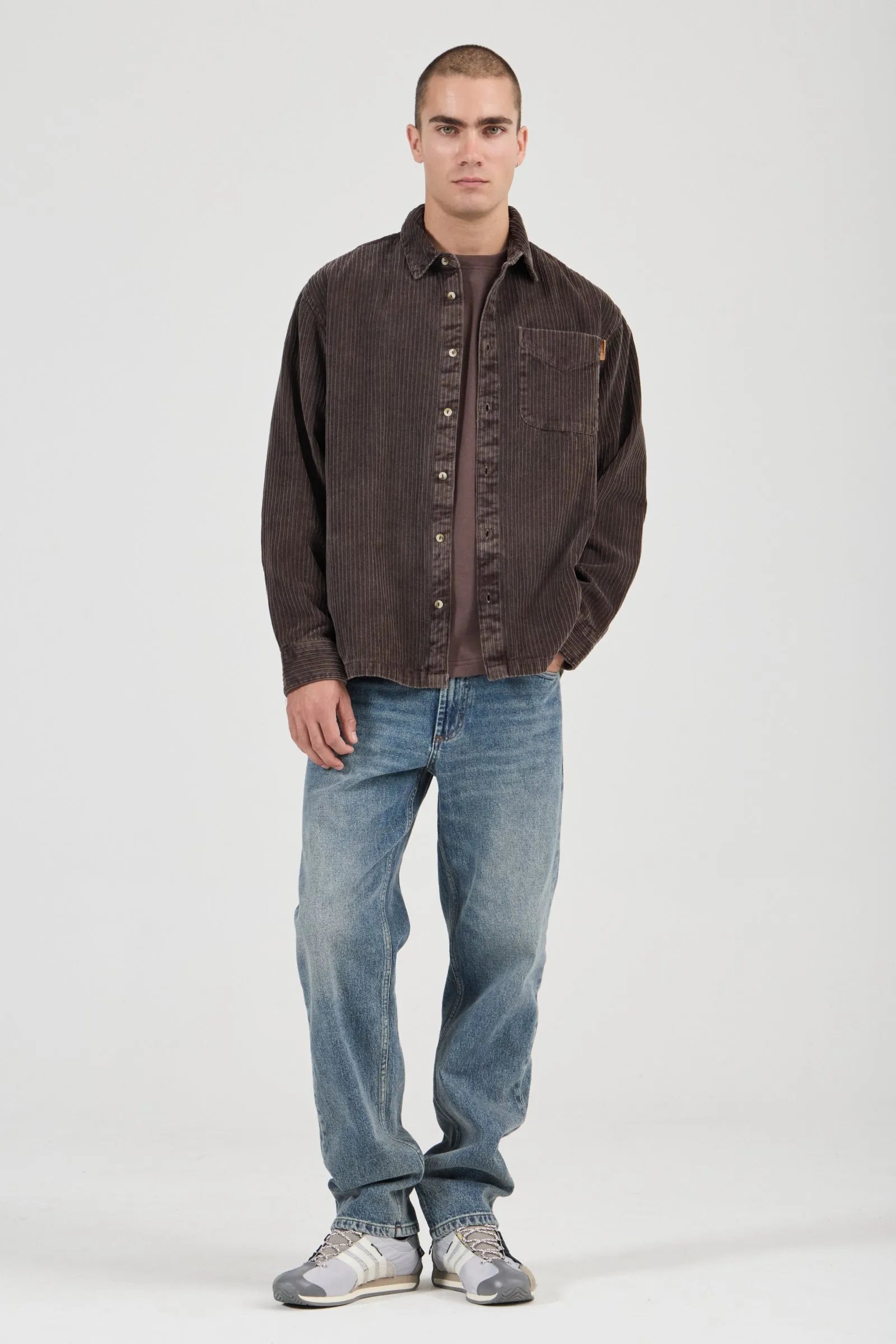 Man wearing a brown button-up shirt and blue jeans on a white background