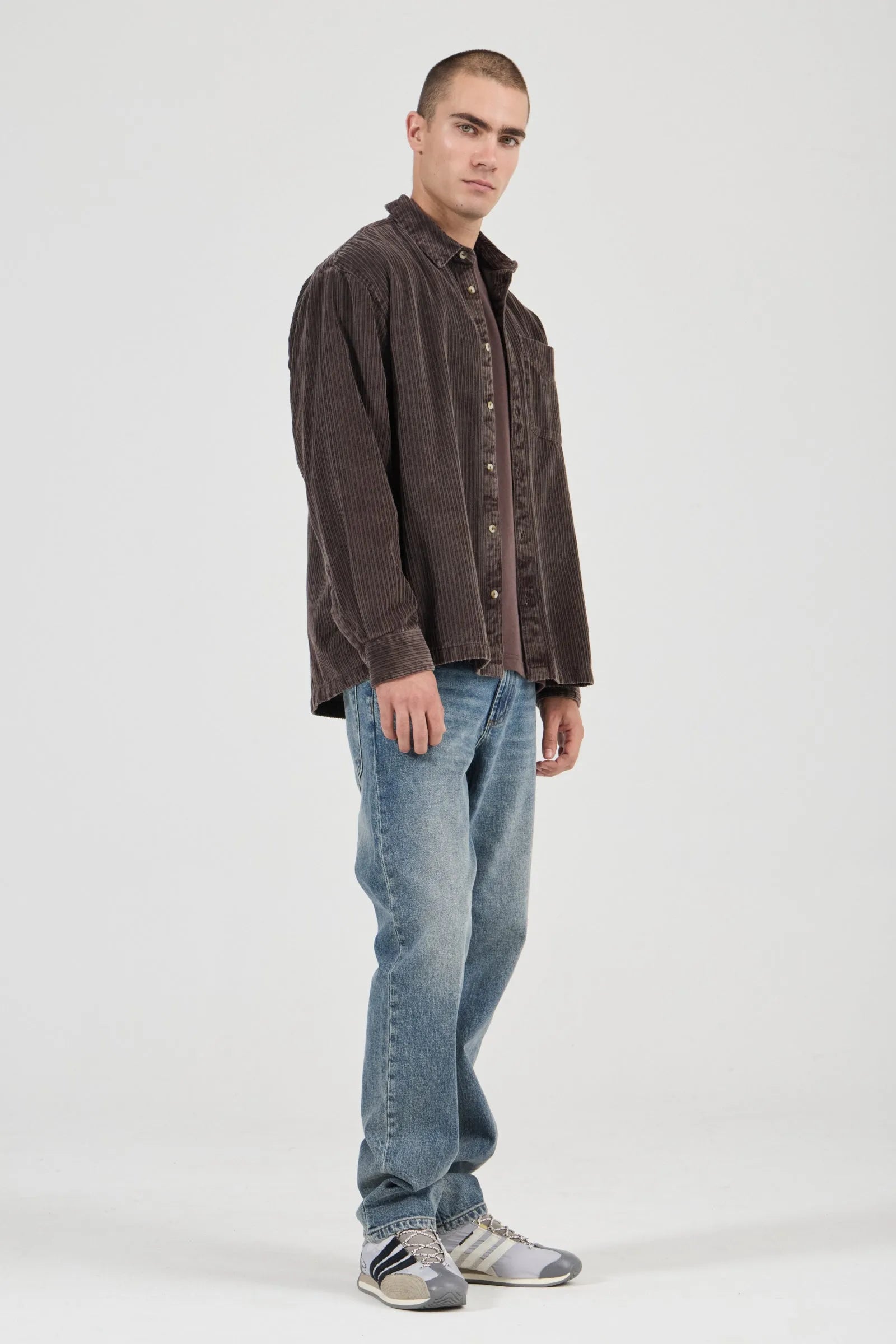 Man wearing a brown shirt and blue jeans on a white background